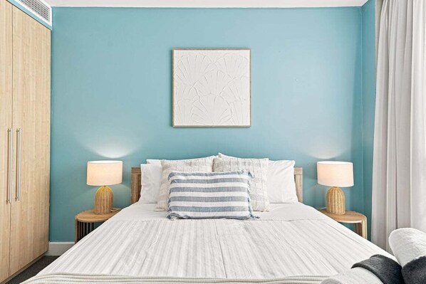 A bedroom with a bed, two bedside tables with lamps, a wardrobe, and a wall-mounted artwork.