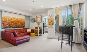 A living room with a red leather sofa, a black chair, a large painting, and a view through a glass door. - Park View Hideaway (Glenelg)