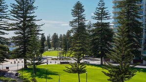 A residential area with tall pine trees, a grassy park, and a multi-story building with balconies. - Park View Hideaway (Glenelg)
