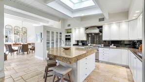 Een moderne keuken met een centraal eiland, witte kasten en een dakraam.