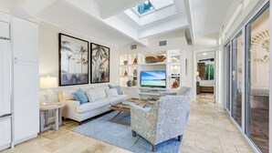 Een ruime woonkamer met een witte bank, een gestreept fauteuil, een flatscreen-televisie en een dakraam.