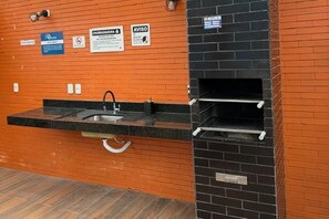 A kitchen with a sink, a black brick oven, and a sign indicating a smoking area. - Fully furnished studio apartment in Maceió with garage, close to the beach and shopping center. (Maceió)
