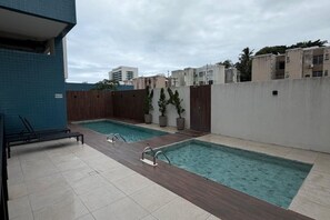 A rooftop pool area with two swimming pools, lounge chairs, and potted plants. - Fully furnished studio apartment in Maceió with garage, close to the beach and shopping center. (Maceió)