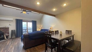 Una habitación con cama, una mesa de comedor con sillas, ventilador de techo, luces empotradas y chimenea.
