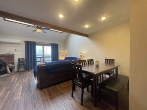 Ein Zimmer mit einem Bett, einem Esstisch mit Stühlen, einem Deckenventilator, Einbauleuchten und einem Kamin.