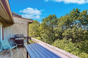 Eine Holzterrasse mit Grill und Stuhl, mit Blick auf einen bewaldeten Bereich.