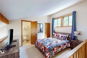 Ein Schlafzimmer mit einem Bett, einem Schreibtisch, einem Fernseher, einem Fenster mit Vorhängen und einer Tür zu einem Badezimmer.