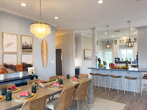 A dining area with wicker chairs, a wooden table, and a chandelier. - 2nd Row Beach | Hot Tub & Game Room | Sleeps 16 (Galveston)