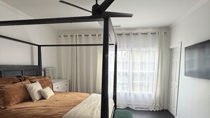 A four-poster bed with a ceiling fan, a bedside table, a green bench, and a large window with curtains. - Lovely 2-bedroom house in vibrant Downtown Atlanta (Atlanta)