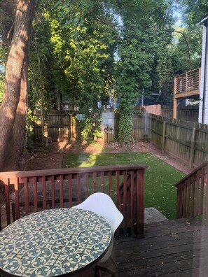 A wooden deck with a patterned table, surrounded by a fenced yard with trees and a wooden structure. - Lovely 2-bedroom house in vibrant Downtown Atlanta (Atlanta)