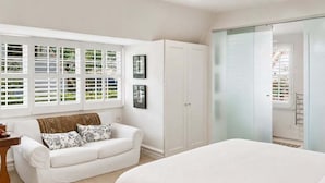 Quarto com cama, sofá branco, guarda-roupa e janela com persianas.