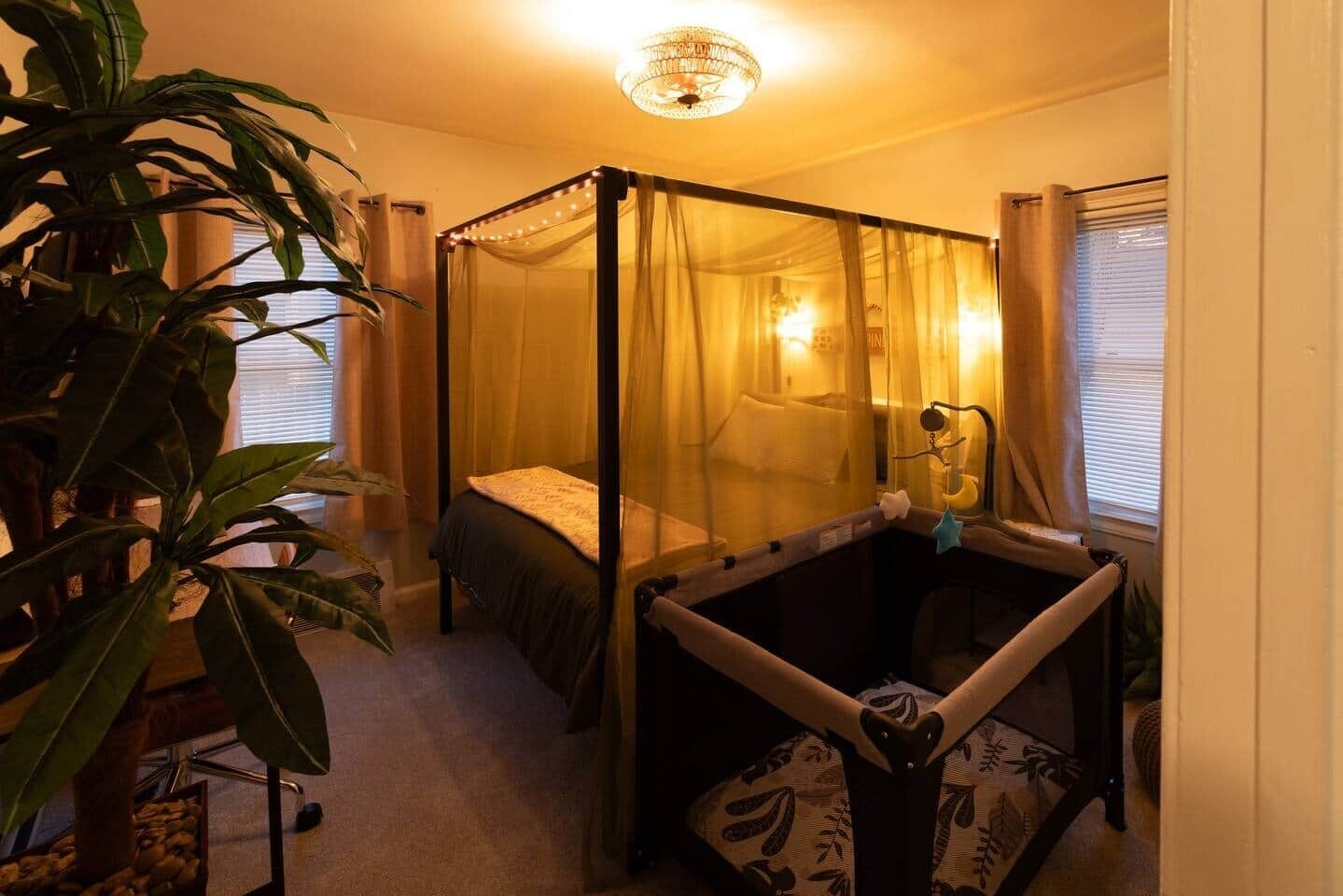 A room with a four-poster bed, a bedside table, a hanging chair, and a large plant.