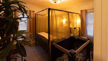 A room with a four-poster bed, a bedside table, a hanging chair, and a large plant.