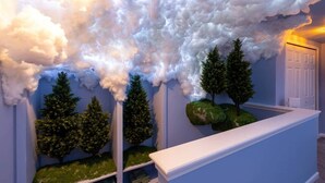 Ein Flur mit Decke in Wolkenform, künstlichen Bäumen und einem weißen Empfangstresen.
