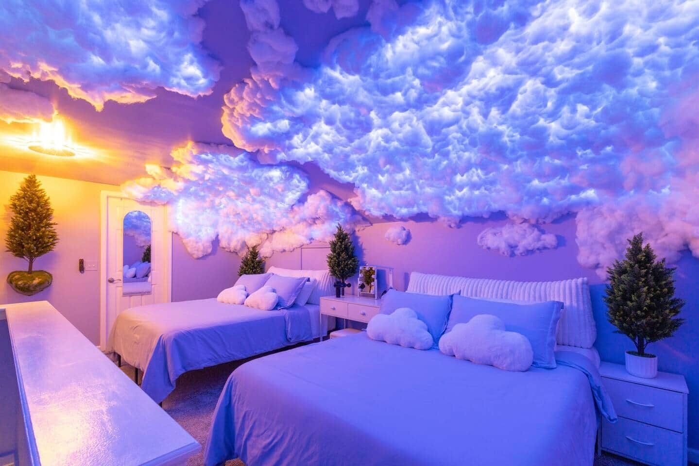 A bedroom with two beds, a bedside table, a nightstand, and a wall with cloud-like decorations.