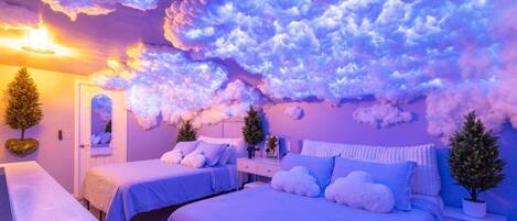 A bedroom with two beds, a bedside table, a nightstand, and a wall with cloud-like decorations.