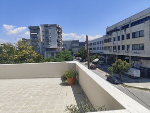 Eine Dachterrasse mit einem Blumentopf, Blick auf eine Stadtstraße mit parkenden Autos und mehrstöckigen Gebäuden im Hintergrund.