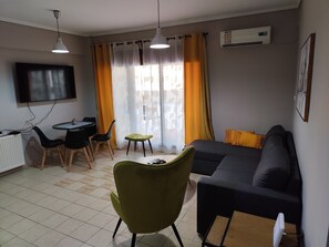 Un salon comprenant un canapé, une table à manger avec des chaises, un téléviseur fixé au mur et un appareil de climatisation.
