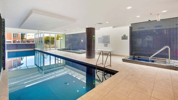 En swimmingpool med klart vatten, ett kaklat golv och en glasvägg som omsluter den.