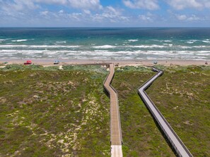 Vista aérea de una zona costera con un muelle de madera largo que lleva a una playa.