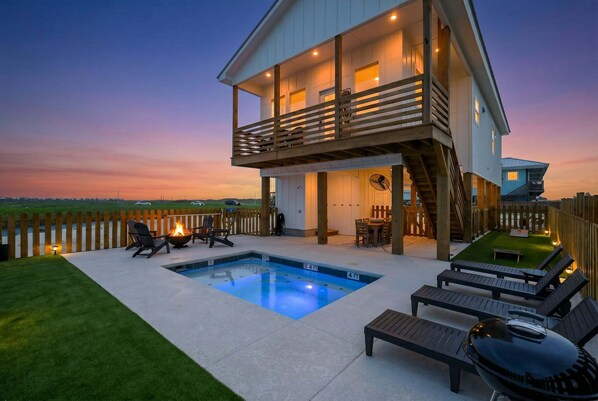 Una casa de dos pisos con piscina, mobiliario exterior y vista al horizonte.