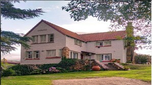 A two-story stone house with a red-tiled roof, a stone staircase, and a well-maintained garden.