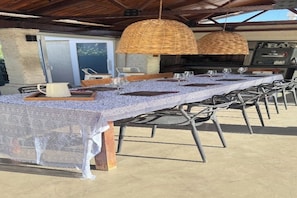 An outdoor dining area with a long table, chairs, and hanging wicker lamps.