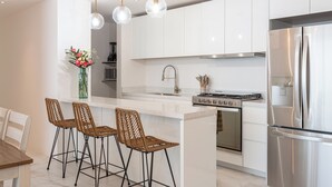 Eine moderne Küche mit weißen Schränken, einem Edelstahlkühlschrank, einem Gasherd und drei Weidenholz-Barhocker.