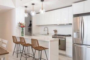 Eine moderne Küche mit weißen Schränken, einem Edelstahlkühlschrank, einem Gasherd und drei Weidenholz-Barhocker.