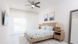 Ein modernes Schlafzimmer mit Bett, Nachttischen, Deckenventilator und Kunstwerken an der Wand.
