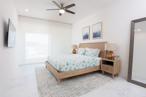 A modern bedroom with a bed, nightstands, a ceiling fan, and artwork on the wall. - Luxury 2BR Condo Walk to Marina & Beach. Access to Pool, Gym & Jacuzzi (Cabo San Lucas)