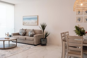 Ein Wohnzimmer mit einer Couch, einem Couchtisch, einem Esstisch mit Stühlen, einer Topfpflanze und Kunstwerken an der Wand.