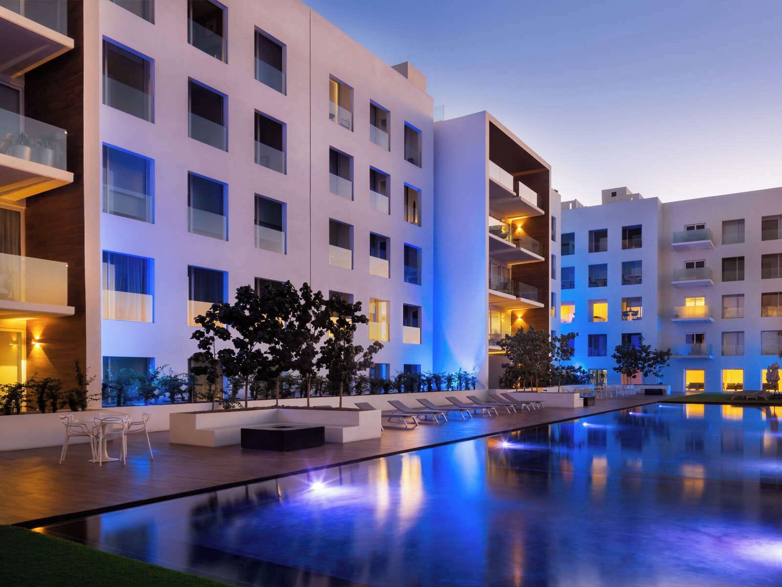 A modern hotel with multiple floors, a swimming pool, and outdoor seating.