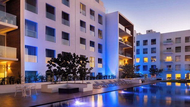 Ein modernes Hotel mit mehreren Etagen, einem Schwimmbad und Sitzgelegenheiten im Freien.
