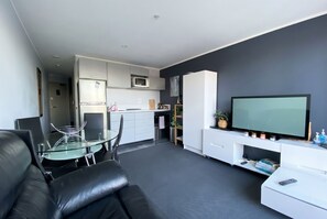 Ein modernes Wohnzimmer mit einer Couch, einem Glastisch, einem Flachbildfernseher, einer Küchenzeile und einem Esstisch.