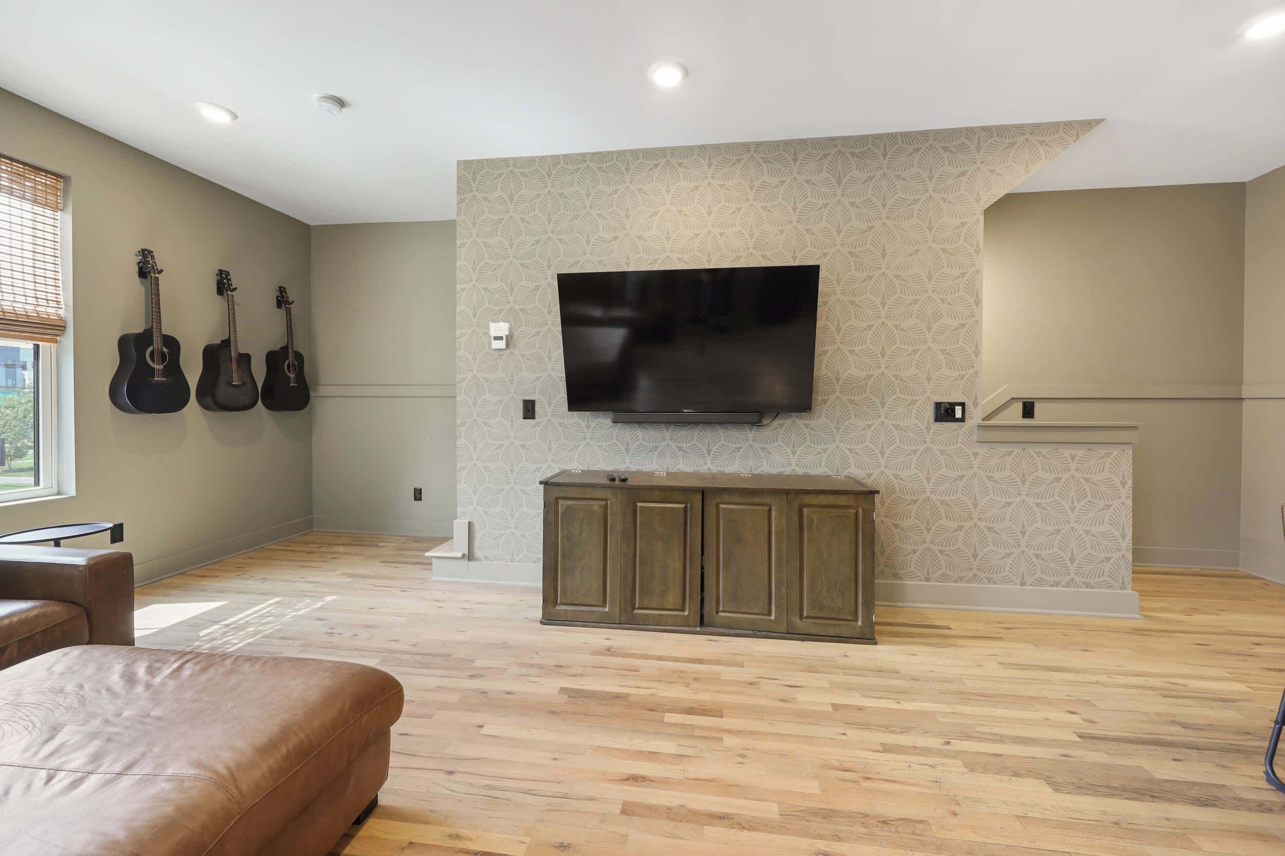 Amplia sala de estar con una gran televisión de pantalla plana montada en una pared con textura, un mueble de madera debajo y tres guitarras colgadas en la pared.