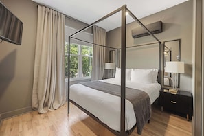 Ein Bett mit Himmelbettgestell aus Holz, ein Nachttisch mit Lampe und ein Fenster mit Vorhängen.
