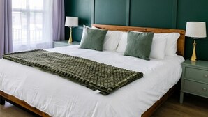 A neatly made bed with white linens, a green throw blanket, and two bedside lamps on a green nightstand. - Cozy 3 Br Cottage, Walk to Hospitals (Tyler)