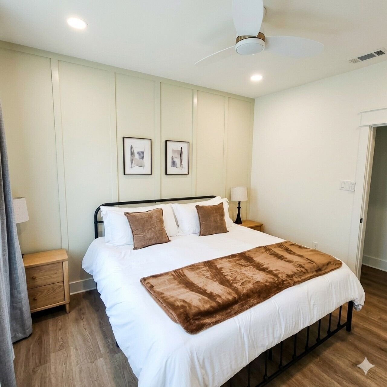 A bedroom with a bed, a nightstand, a lamp, a ceiling fan, and framed pictures on the wall.