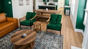 A modern living room with a sofa, chairs, a coffee table, and a kitchen in the background. - Cozy 3 Br Cottage, Walk to Hospitals (Tyler)
