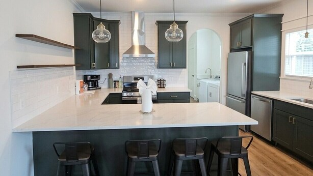 A modern kitchen with a large island, dark cabinets, pendant lights, and a stainless steel refrigerator. - Cozy 3 Br Cottage, Walk to Hospitals (Tyler)
