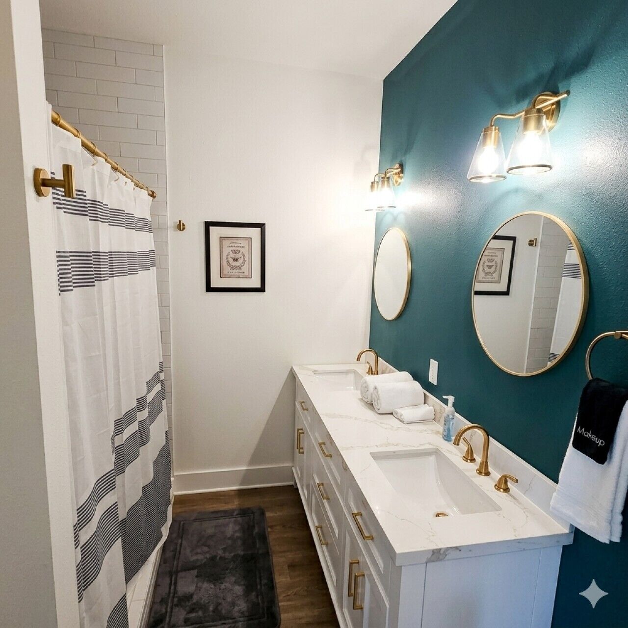 Un baño con tocador blanco, dos lavamanos, accesorios dorados, una pared de acento color aguamarina, una cortina de ducha y un certificado enmarcado en la pared.