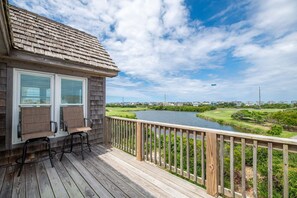 Eine Holzterrasse mit zwei Stühlen und einem Fenster mit Blick auf einen Fluss und einen Golfplatz.