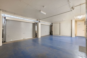 A spacious indoor area with two closed roller doors and a flat, unadorned floor. - Salt & Skyline Penthouse (Holdfast Bay)
