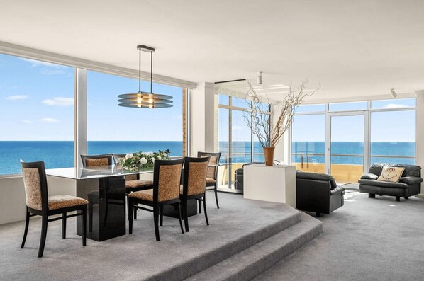 A modern interior with a dining area, sofas, and large windows overlooking the sea. - Salt & Skyline Luxury Penthouse in Glenelg (Holdfast Bay)