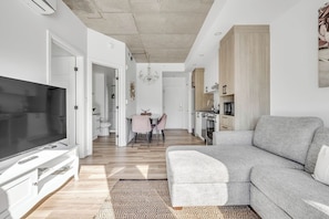 Un salon moderne avec un canapé gris, un téléviseur à écran plat et un coin repas comprenant une table et des chaises.