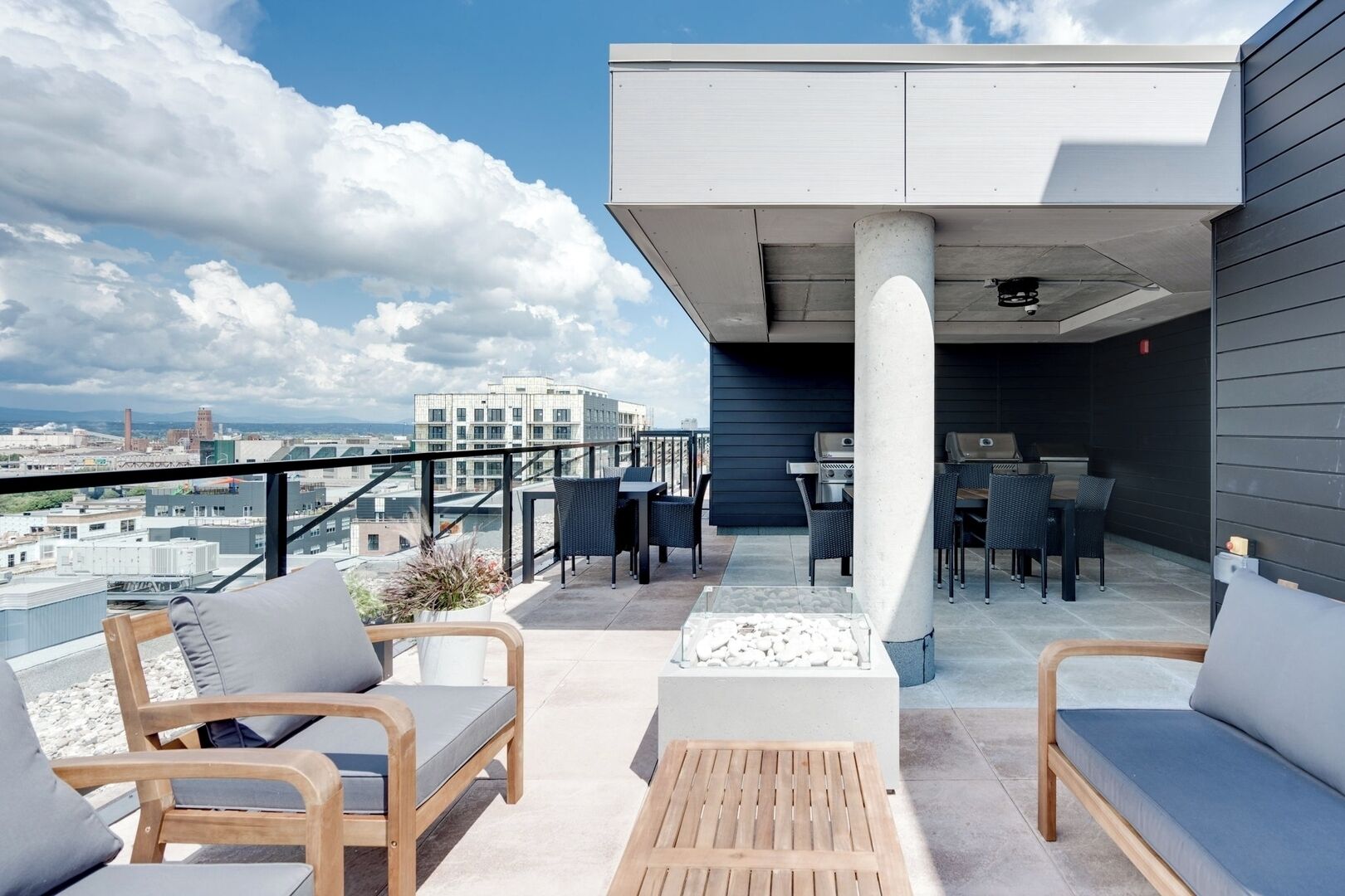 A rooftop terrace with outdoor seating, a grill, and a view of the cityscape.
