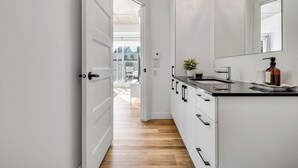 Une cuisine moderne avec des meubles blancs, un plan de travail noir et un miroir au-dessus de l’évier.