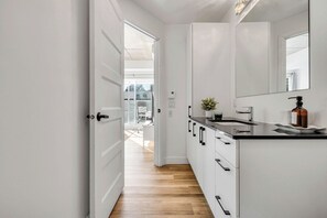 Une cuisine moderne avec des meubles blancs, un plan de travail noir et un miroir au-dessus de l’évier.