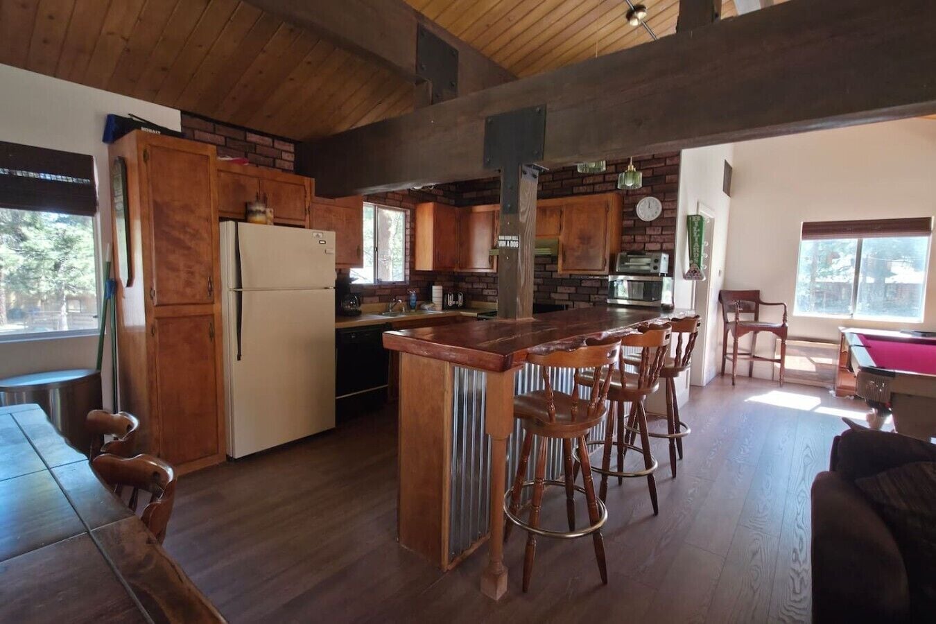 Una cocina amplia con armarios de madera, una isla central con taburetes de bar, un refrigerador y una mesa de comedor.